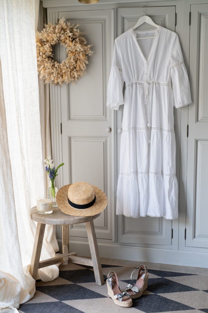 No.Eleven white kaftan hanging up next to a straw hat and Tabitha Simmons wedge sandals